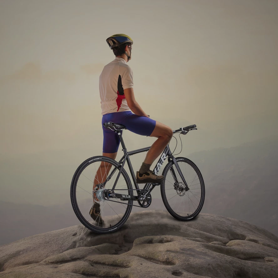 Cyclist in white and red jersey and blue shorts riding a dark gray WAR bike on a rocky overlook, hazy mountain backdrop