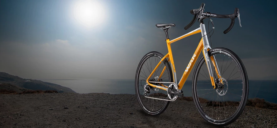 Yellow and silver gravel bike on a rocky coastal cliff at sunset, sea and hazy sun in background