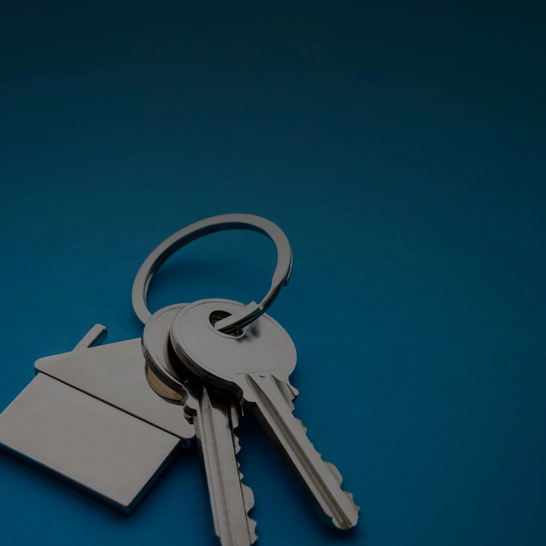 Silver house-shaped keychain with two metal keys on a split ring, resting on a deep blue background, no on-image text