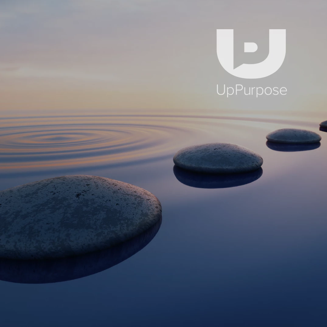 UpPurpose logo in white over stepping stones on calm water at dusk, rippling reflections, muted blue and lavender tones