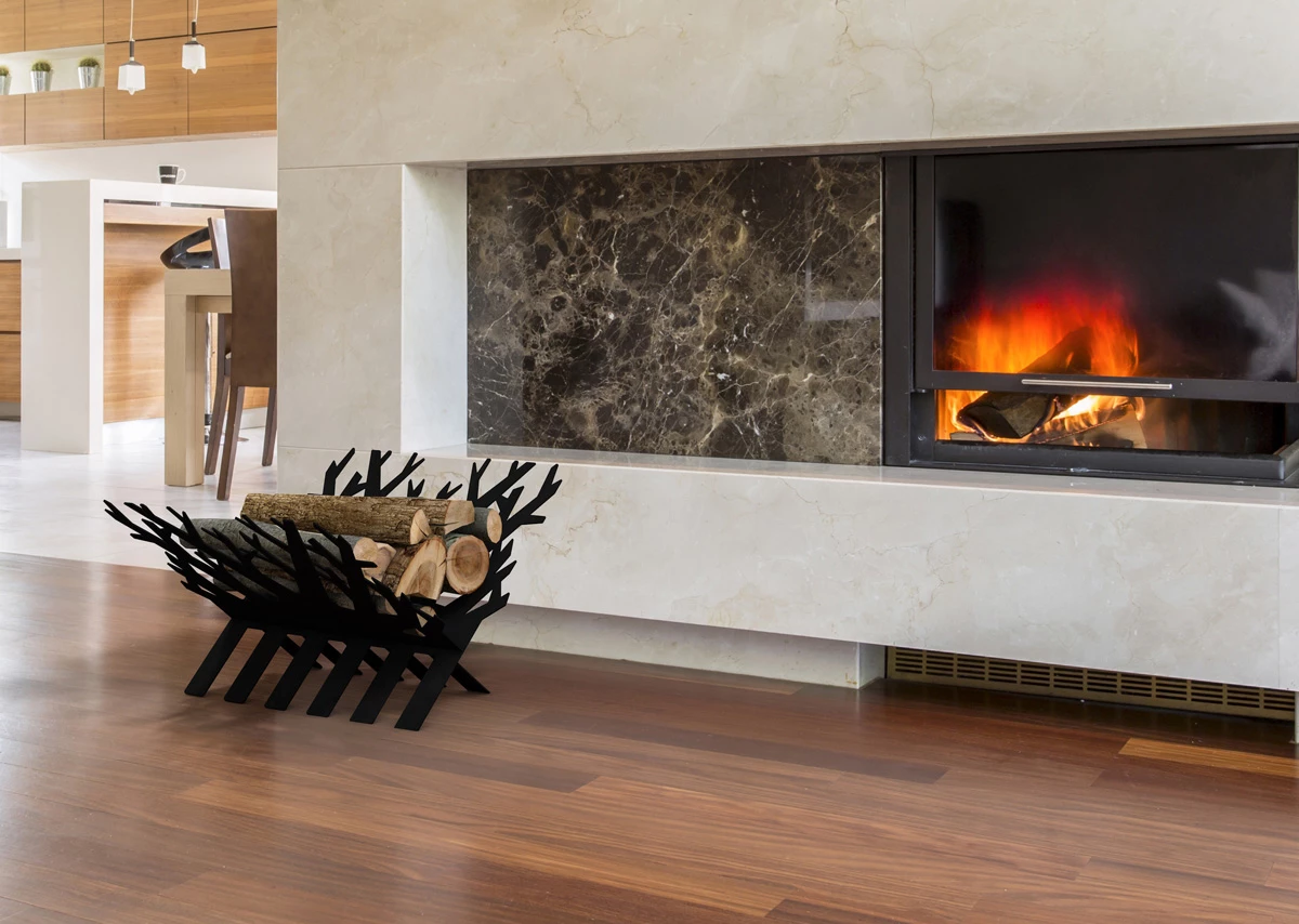 Black branch-style metal log rack holding firewood beside a built-in fireplace with lit fire, marble and wood interior