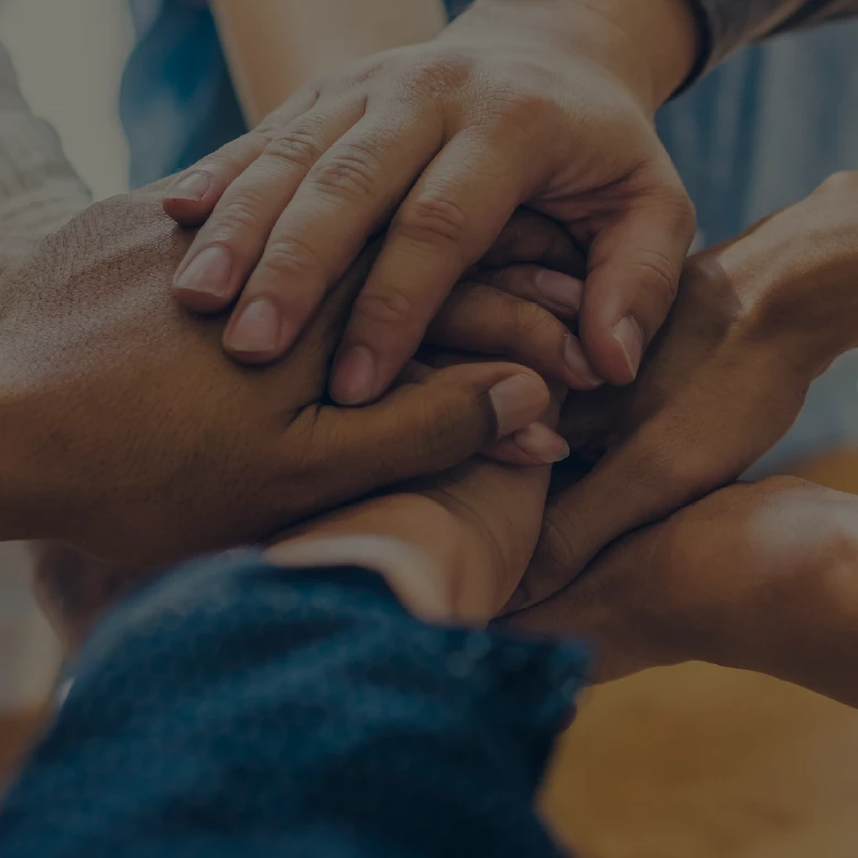 Multiple hands stacked together in a huddle, teamwork and unity lifestyle photo, dark moody overlay, no on-image text
