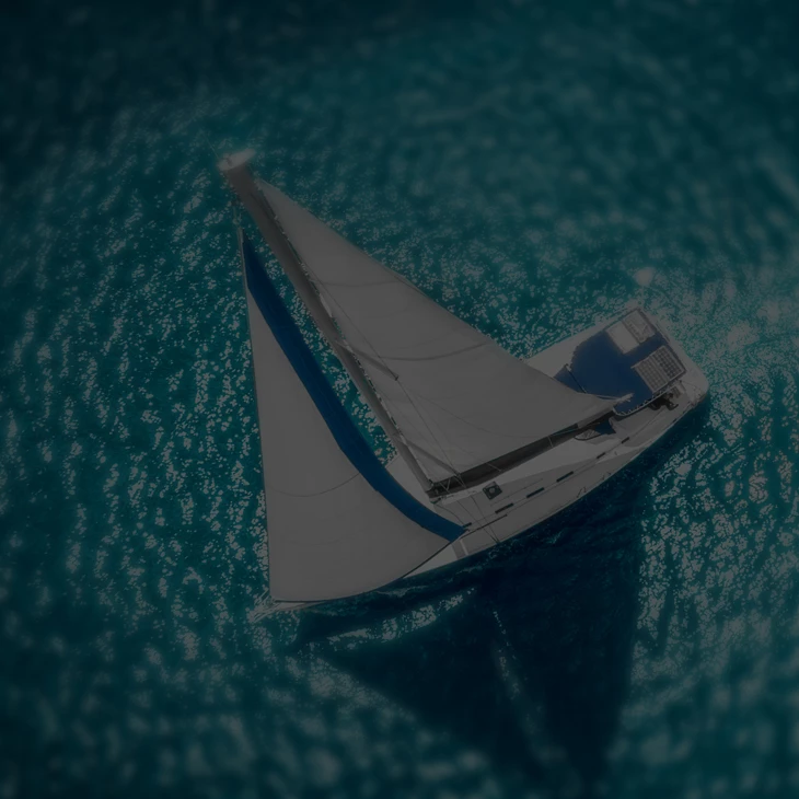 Aerial top-down photo of a white sailboat with blue sail trim sailing on dark teal ocean water, moody dimmed overlay